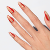 Angled photo of light skinned hand with Red Accent with Gems Nails