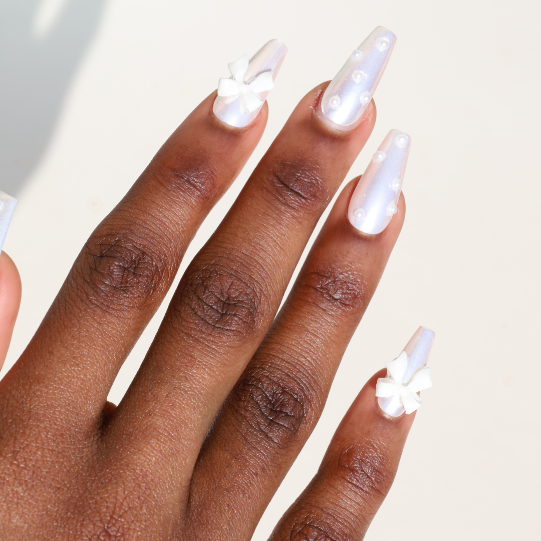 Angled photo of dark skinned hand with White Chrome 3D Bow Pearl Nails