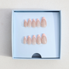 Dark skinned hand with Pearl Nude French Tip Nails in packaging