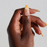 Dark skinned thumb with Orange Chrome Moderne Nails